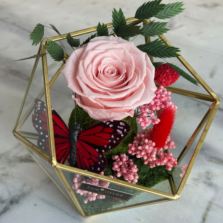 Eternal rose named Raegan by ESOR ATELIER, featuring a preserved, vibrant red rose in a glass display.